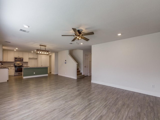 unfurnished living room featuring dark wood-style floors, visible vents, stairway, and baseboards