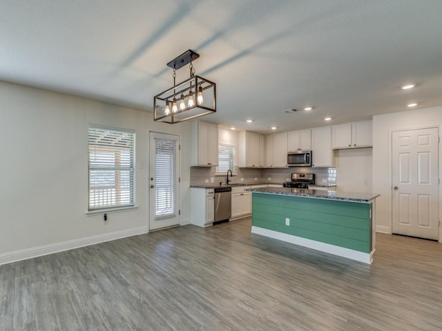 kitchen featuring wood finished floors, baseboards, stainless steel appliances, decorative backsplash, and white cabinetry