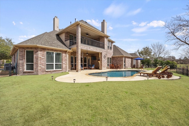 back of property with a balcony, a ceiling fan, fence, and a chimney