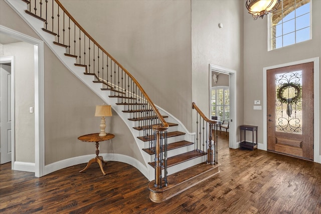 entryway with stairs, wood finished floors, baseboards, and a towering ceiling