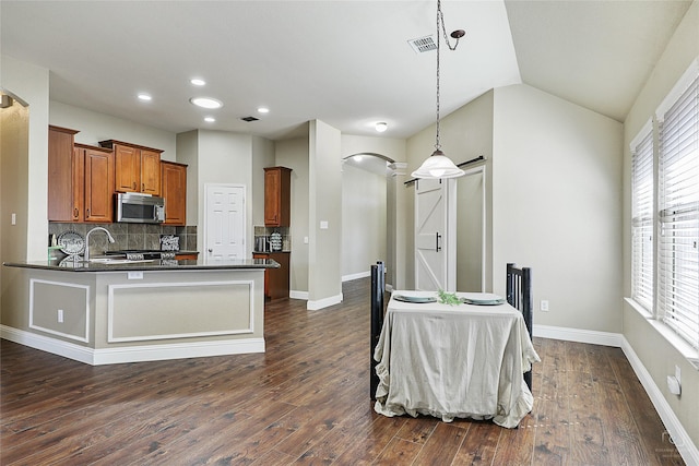 kitchen featuring brown cabinetry, stainless steel microwave, dark wood finished floors, and tasteful backsplash