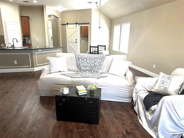 living area featuring dark wood-style floors, baseboards, arched walkways, vaulted ceiling, and a barn door