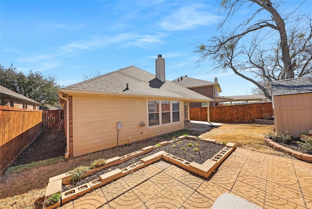 rear view of property featuring a shingled roof, a fenced backyard, a chimney, and a patio area