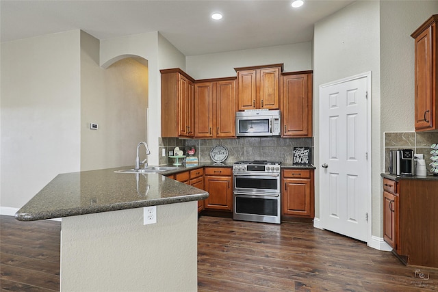 kitchen with a sink, stainless steel appliances, dark wood-type flooring, and a peninsula