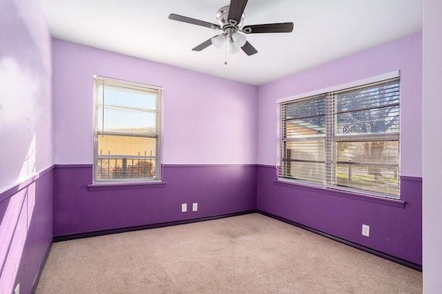 carpeted empty room featuring a wainscoted wall, a healthy amount of sunlight, and ceiling fan