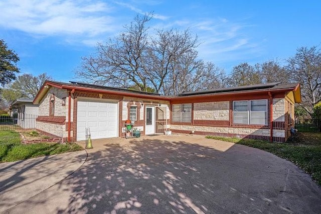 view of front facade with roof mounted solar panels, concrete driveway, an attached garage, and fence