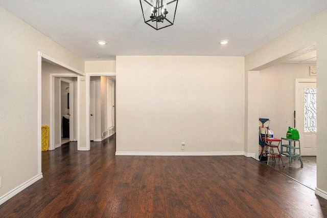 unfurnished room with a notable chandelier, baseboards, and wood finished floors