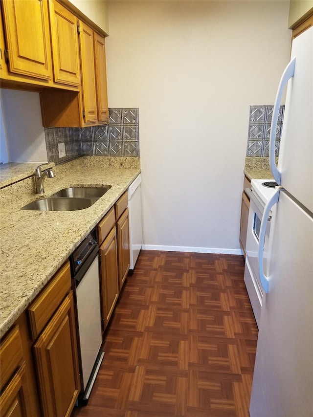 kitchen featuring baseboards, light stone counters, decorative backsplash, white appliances, and a sink
