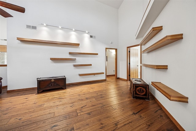 unfurnished living room featuring visible vents, a ceiling fan, hardwood / wood-style flooring, a high ceiling, and baseboards