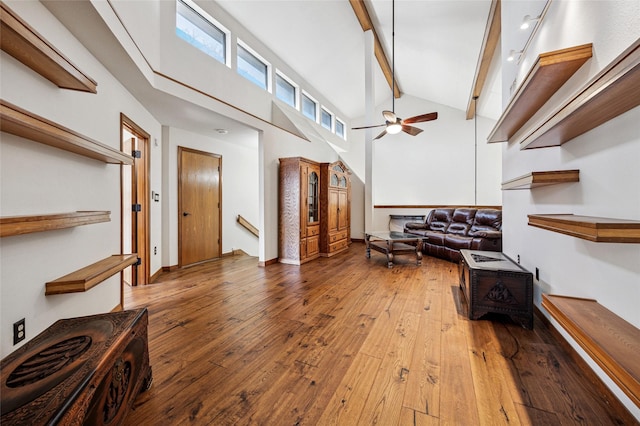 sitting room with baseboards, high vaulted ceiling, ceiling fan, wood-type flooring, and beamed ceiling