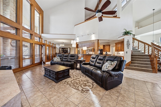 living area featuring a wealth of natural light, light tile patterned flooring, stairs, and ceiling fan with notable chandelier