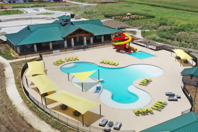 pool with a patio area, a water play area, a water slide, and fence