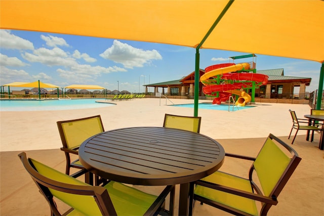 view of patio / terrace with a water play area, outdoor dining space, a community pool, and fence