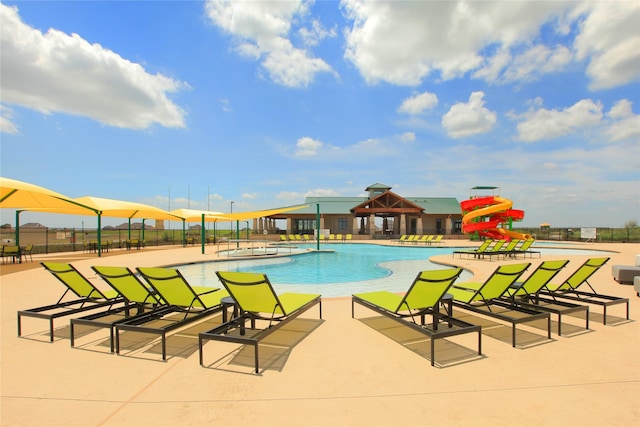 community pool with a patio area, a water slide, a water play area, and fence