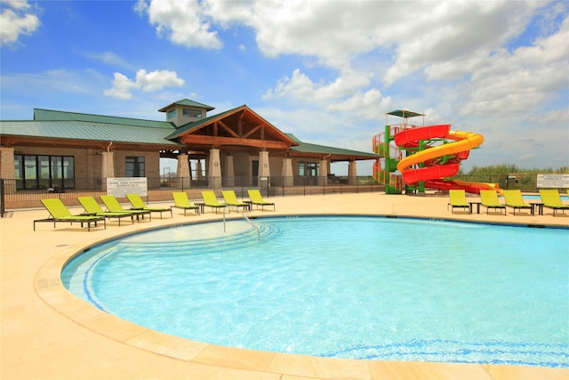 community pool with a patio, a water slide, and fence