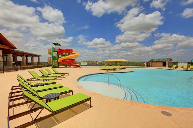 community pool with a patio, fence, and a water slide