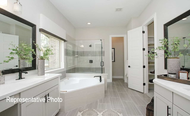 full bath with visible vents, two vanities, a sink, a shower stall, and a garden tub