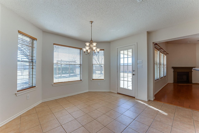 unfurnished dining area with light tile patterned floors, a chandelier, plenty of natural light, and a fireplace