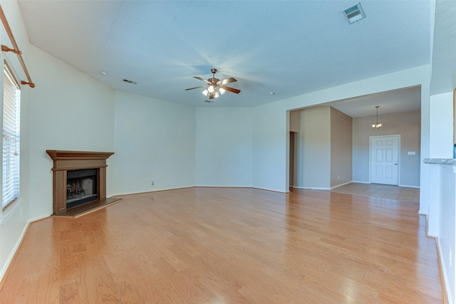 unfurnished living room featuring light wood-type flooring, visible vents, a fireplace with raised hearth, and a ceiling fan