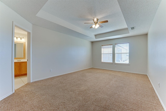 unfurnished room featuring visible vents, ceiling fan, light carpet, a textured ceiling, and a raised ceiling