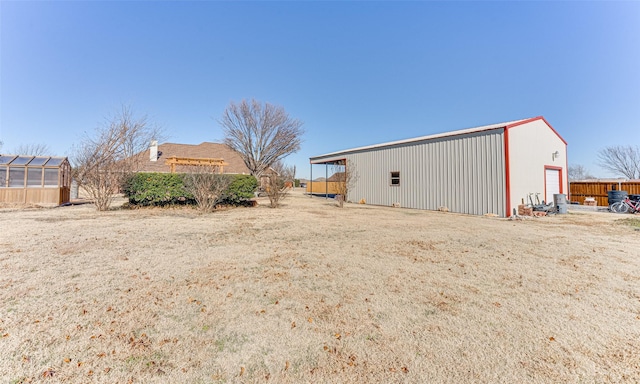 view of yard featuring an outbuilding, fence, a greenhouse, a pole building, and a garage