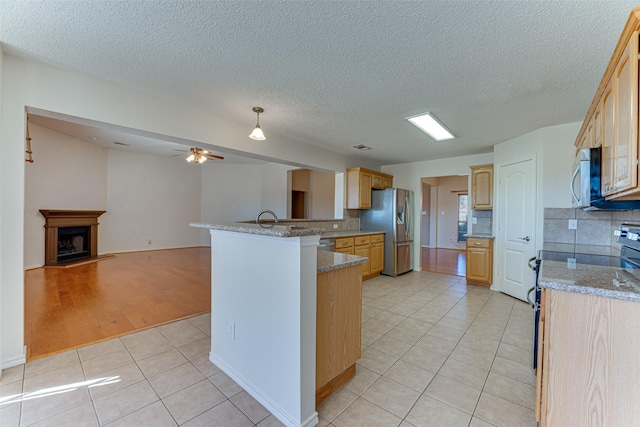 kitchen with light tile patterned floors, light brown cabinetry, stainless steel appliances, open floor plan, and backsplash