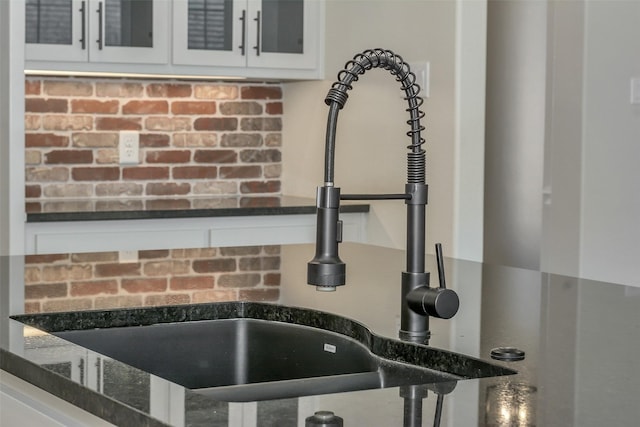 details with a sink, glass insert cabinets, white cabinets, and dark stone counters