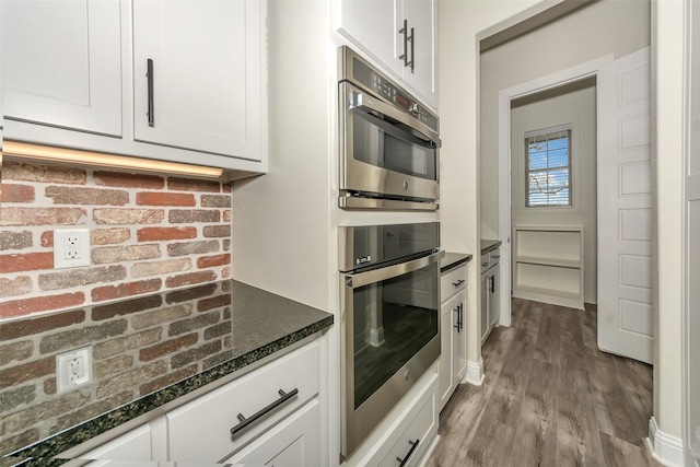 kitchen featuring dark stone countertops, wood finished floors, double oven, and white cabinets