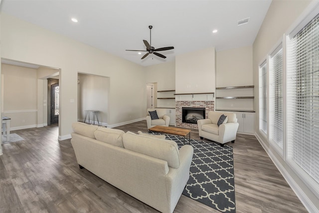 living area with dark wood finished floors, recessed lighting, baseboards, a brick fireplace, and ceiling fan