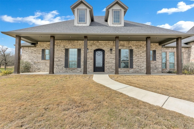 view of front of home with a front yard, brick siding, and roof with shingles