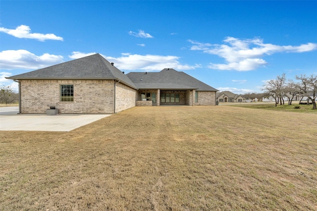 back of house featuring brick siding, a lawn, a patio, and roof with shingles