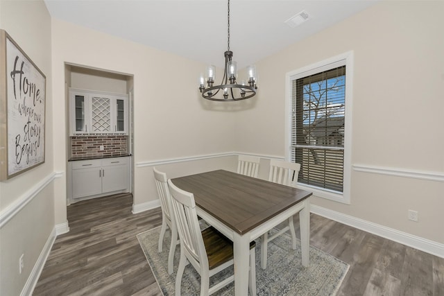 dining space featuring dark wood finished floors, baseboards, visible vents, and a chandelier