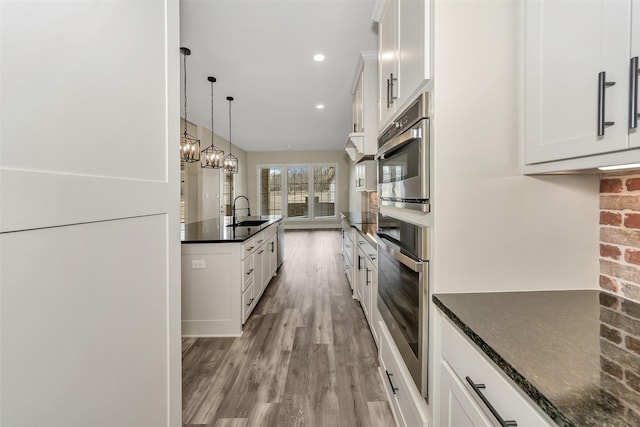 kitchen with oven, light wood-type flooring, white cabinetry, and a sink