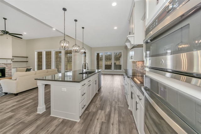 kitchen featuring ceiling fan with notable chandelier, a sink, a kitchen breakfast bar, wood finished floors, and white cabinetry