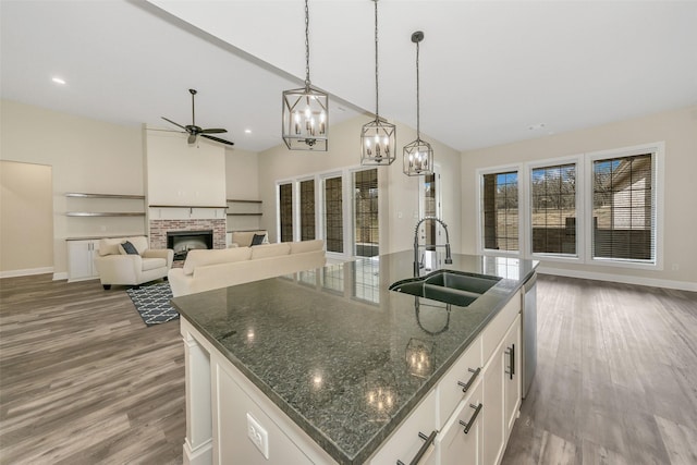 kitchen featuring ceiling fan with notable chandelier, a fireplace, wood finished floors, and a sink