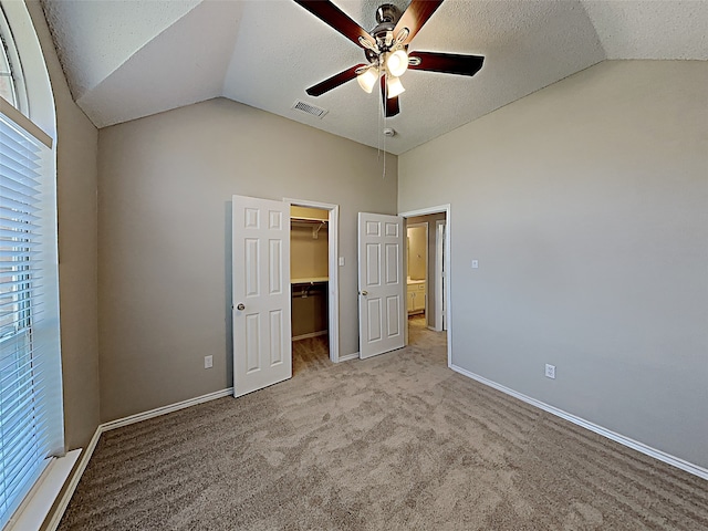 unfurnished bedroom featuring visible vents, carpet floors, lofted ceiling, a spacious closet, and a textured ceiling