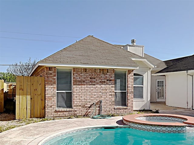 back of house featuring brick siding, an outdoor pool, an in ground hot tub, and a chimney