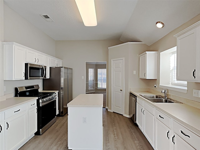 kitchen featuring lofted ceiling, a sink, stainless steel appliances, white cabinets, and a center island