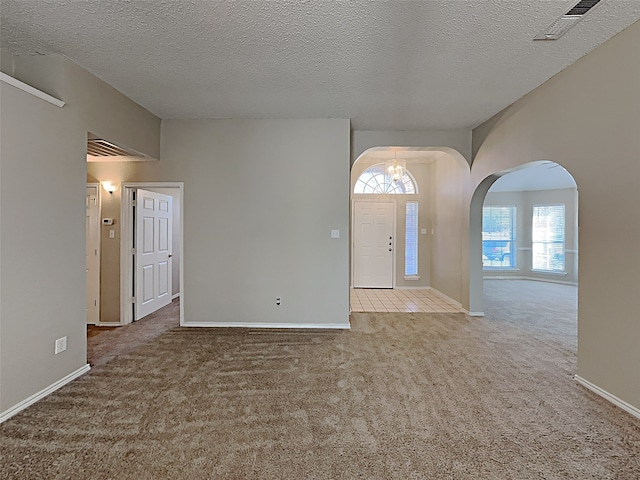 carpeted spare room featuring arched walkways, visible vents, a textured ceiling, and baseboards