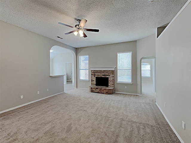 unfurnished living room featuring visible vents, a fireplace, arched walkways, ceiling fan, and carpet flooring