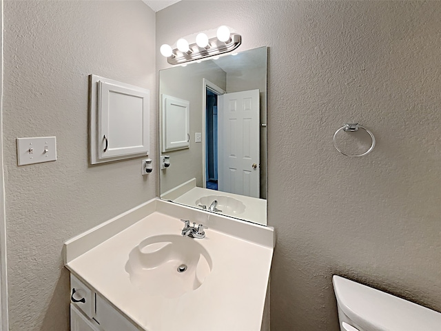 half bathroom featuring toilet, vanity, and a textured wall