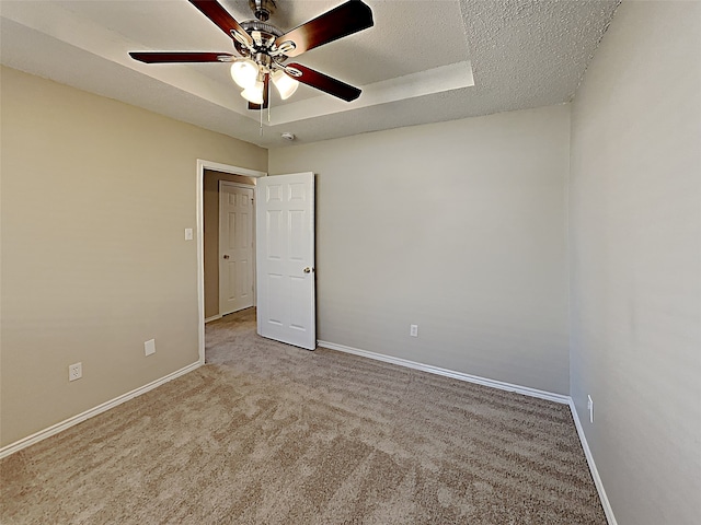 carpeted empty room with a tray ceiling, a ceiling fan, baseboards, and a textured ceiling