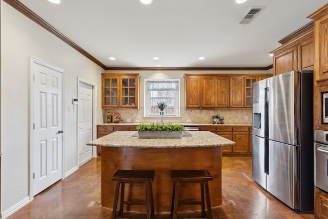 kitchen with visible vents, a kitchen breakfast bar, backsplash, stainless steel appliances, and brown cabinetry