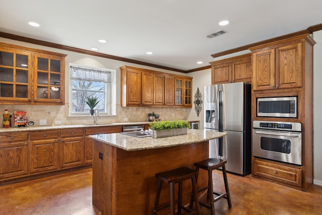 kitchen featuring backsplash, a kitchen bar, brown cabinetry, stainless steel appliances, and a sink