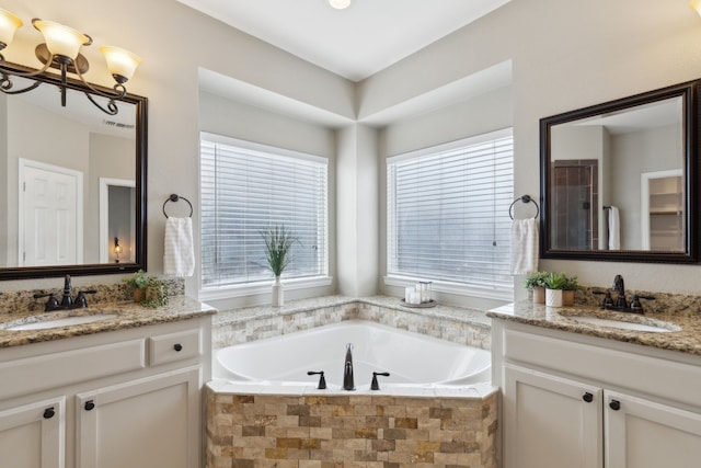 bathroom with a garden tub, a notable chandelier, two vanities, and a sink