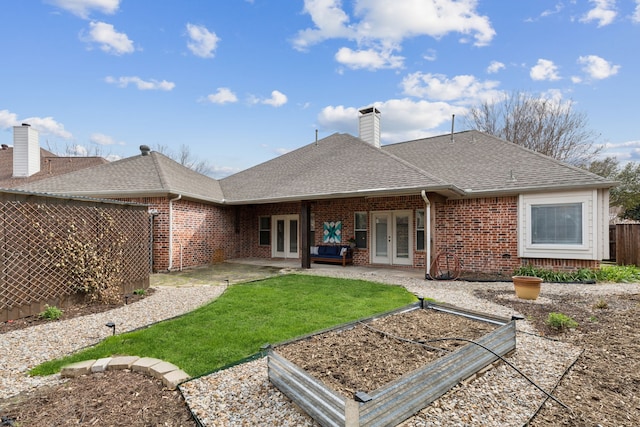 back of property featuring fence, french doors, roof with shingles, a vegetable garden, and brick siding