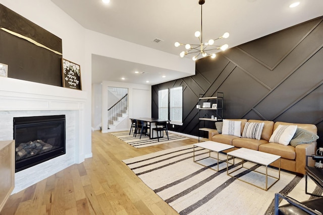 unfurnished living room featuring stairway, wood finished floors, visible vents, a glass covered fireplace, and a notable chandelier