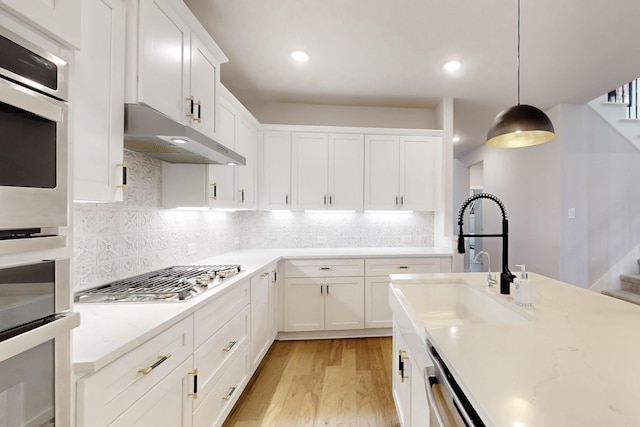 529 Hummingbird Dr, Celina, TX 75009 - kitchen with white cabinetry, under cabinet range hood, light wood finished floors, and appliances with stainless steel finishes