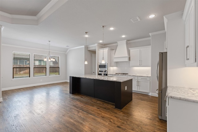 kitchen featuring premium range hood, an island with sink, ornamental molding, a sink, and backsplash