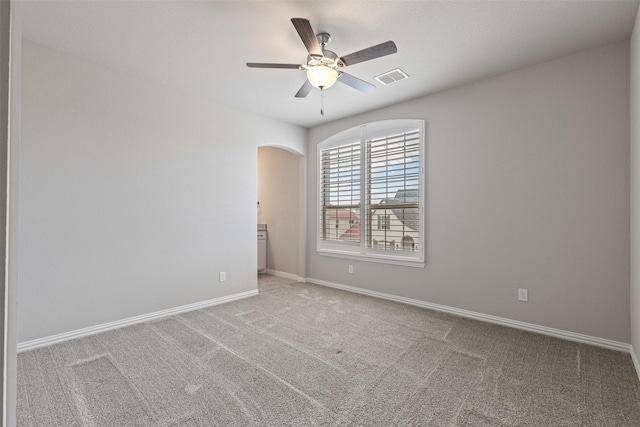 carpeted empty room featuring visible vents, arched walkways, baseboards, and ceiling fan